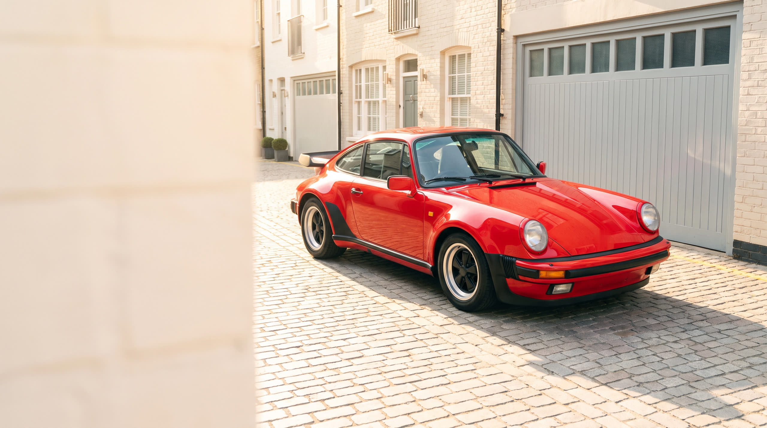 A gleaming red classic sports car in a bright London mews at morning